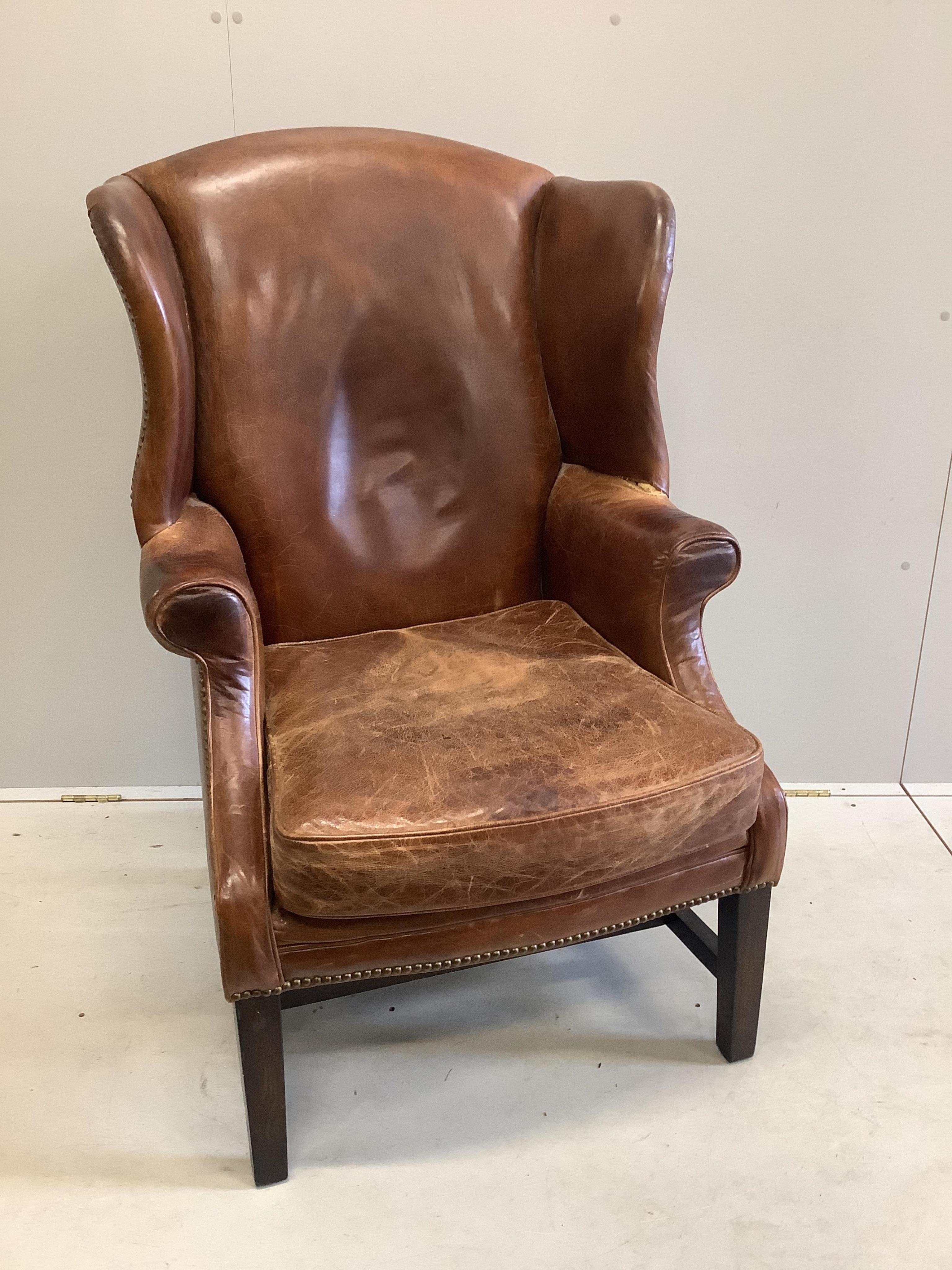 A George III style oak and tan leather wing back armchair, width 76cm, depth 70cm, height 112cm. Condition - poor to fair